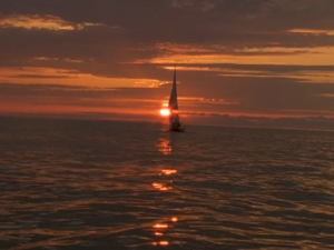 A wide shot of Pacey's boat sailing off into a beautiful orange sunset.