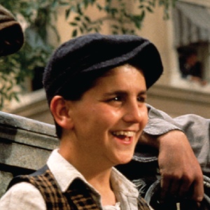 Max Casella, wearing a newsies cap and vest and cracking a grin