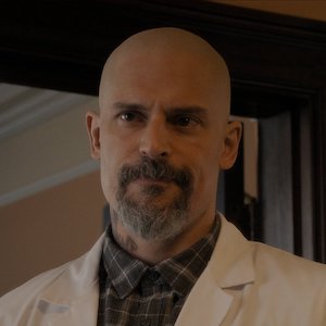 Joe Manganiello, a bald man with a salt and pepper beard wearing a plaid shirt and white jacket