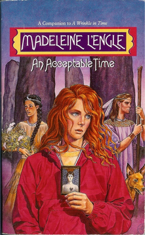 A red-headed girl in a red windbreaker holds a picture of a man with two people standing behind her in front of a bunch of stone pillars.