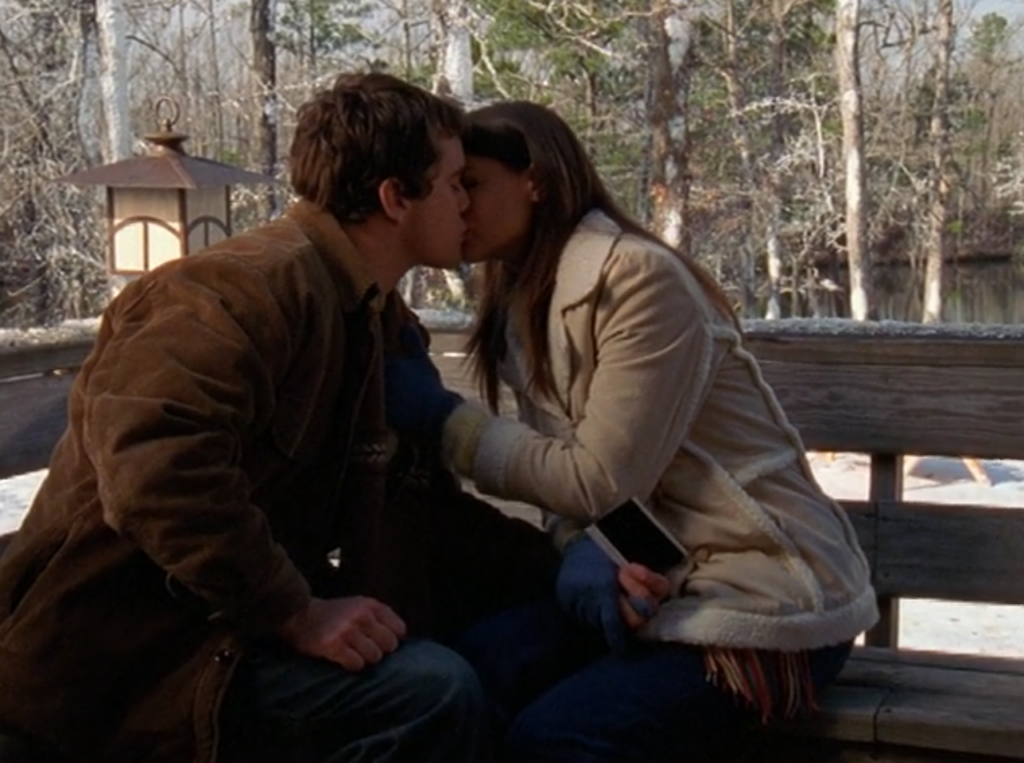 Pacey and Joey sit outside on a bench in the snow, kissing