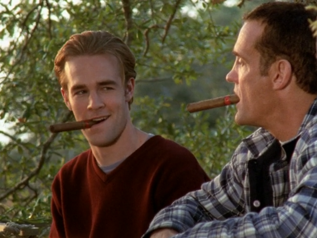 Dawson and his dad sit in the woods, chewing unlit cigars and smiling at each other