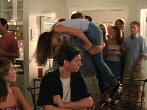 Pacey carries joey over his shoulder from a party while Drue Valentine looks on