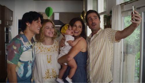 Photo of Danny Ramirez, Lili Reinhart, Andrea Savage holding a baby, and Luke Wilson holding out a phone to take a selfie of the group