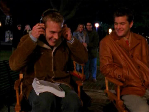 Dawson and Pacey sit next together on a film set, in director's chairs in the snow, with Dawson leaning forward in a headset, very directorially