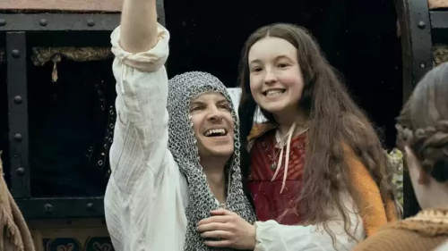 Andrew Scott, a white man wearing chain mail on his head, hoisting up a grinning young white girl (Bella Ramsey) 