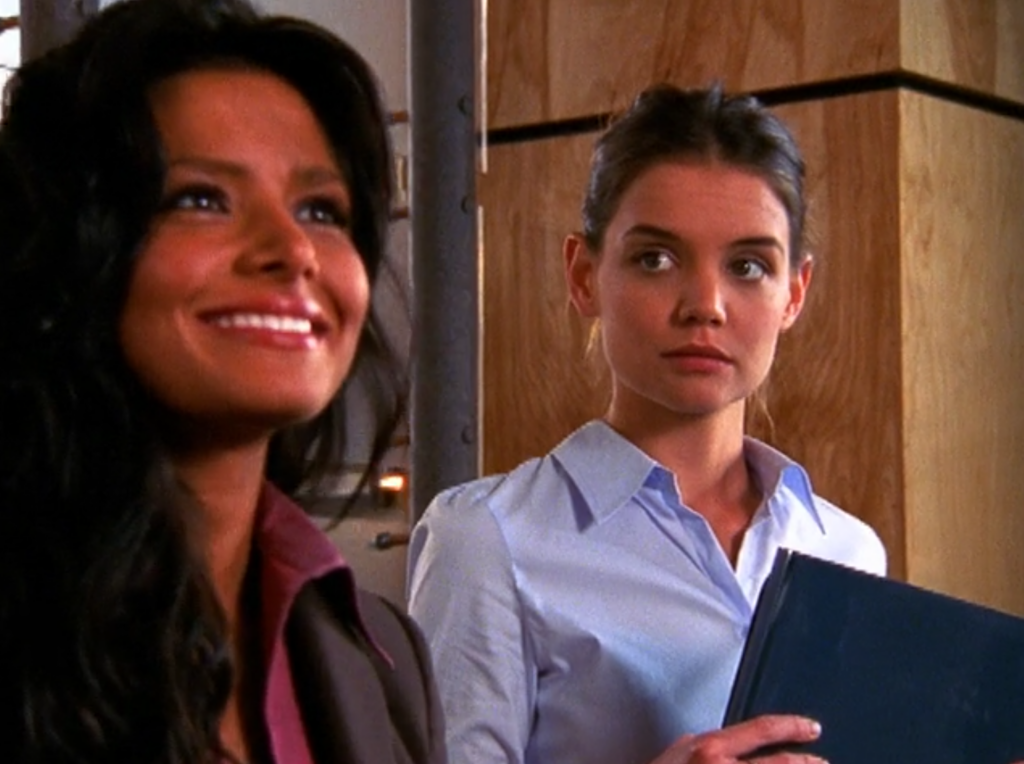 Joey, dressed in office attire, looks jealously at a beautiful woman sitting next to her, who is smiling at Pacey (off-camera)