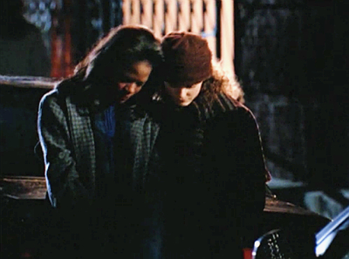 Elena and Felicity sit together outside in the dark, both looking down with their heads tilted together and Felicity's arm sweetly around Elena