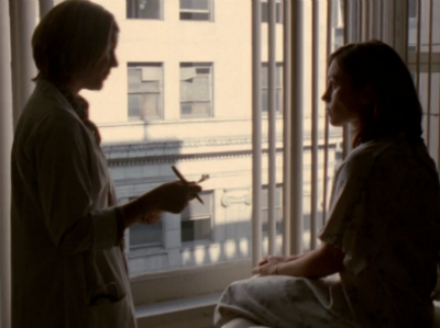 A silhouette of Julie in the health center, sitting by a window while a doctor asks her questions.