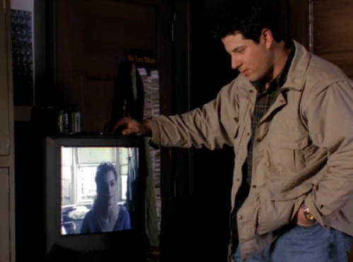 Sean stands next to a TV with Felicity's face on it, looking down at his creation
