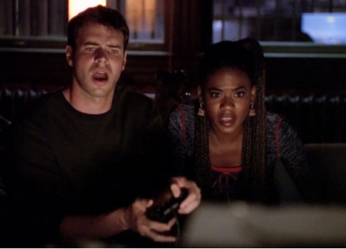 Noel and Elena play a video game together, both looking disheveled and obsessed