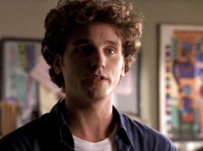 Chris William Martin as Greg, with extremely fluffy curly hair