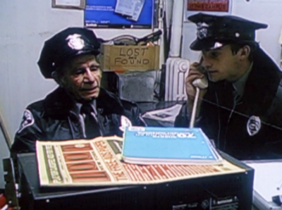 Ben in a security guard uniform on the phone, next to a grizzled old security guard