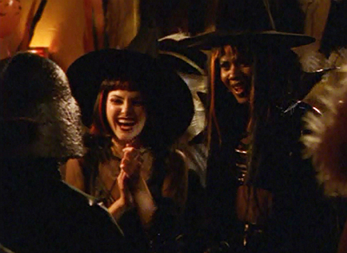 Felicity and Elena, both dressed up as witches with cool wigs and pointy hats, crack up together at a costume party