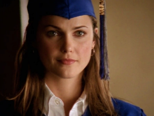 Felicity, in a blue graduation cap and grown, stares just off camera with a proud look on her face