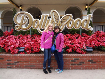 Sarah and Meredith, both in hot pink jackets, standing in front of the Dollywood sign together, smiling