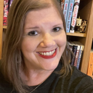 A white blonde woman smiling with a book shelf in the background