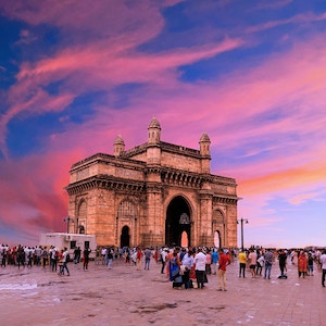 The Gateway to India archway in Mumbai, India, in front of a pink and blue sunset