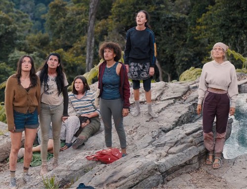 A group of teen girls, looking dirty and worn, standing on a rock