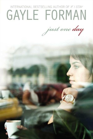 Cover of Just One Day, with a white girl with brown hair stares out of the window at a European building with her hand (big watch on her wrist) under her chin and a cup of coffee in the other hand