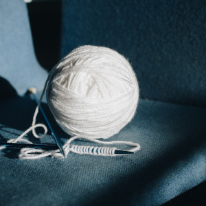 A ball of white yarn with knitting needles attached