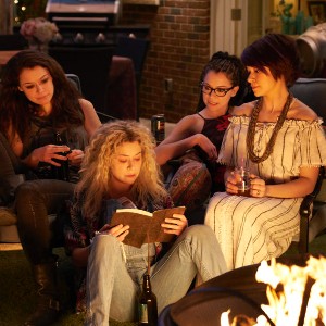 A still from Orphan Black, with four clones of the same woman sitting together by a fire