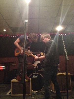 Two young white guys rocking out on guitar together
