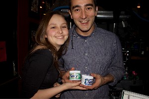 A young woman and young man, smiling and each holding a tin of gum