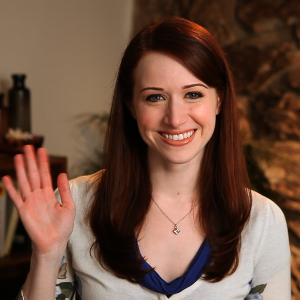 An auburn-haired white woman waves at the camera