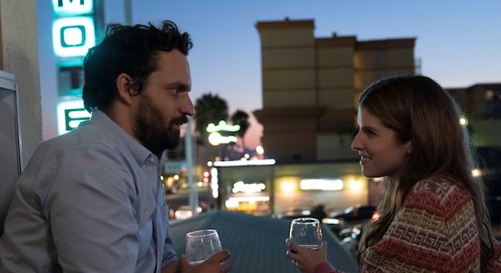 A white man with brown hair and a beard looks at a white woman with brown hair while drinking wine