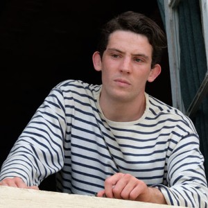 A white young man with short brown hair and slightly large ears stares out from a window