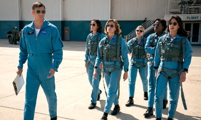 A male instructor in a flight suit escorts five pilots in flight suits.