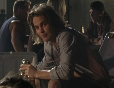Tim Riggins, a white teenage boy with long shaggy brown hair and a smirk, reaching into a cooler of beer