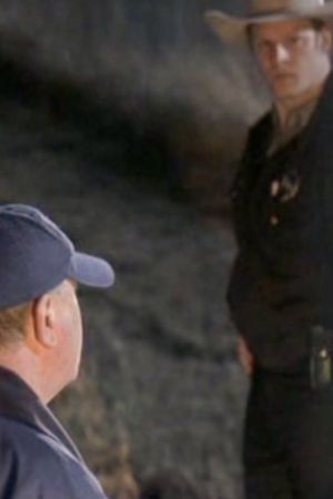 A cop and a football coach stand outside of a bus on the side of the road.