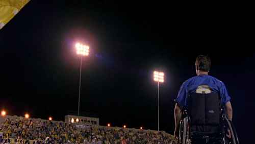 Jason Street sits in his wheelchair, back to camera, overlooking the enormous crowd of Panther fans for the homecoming game