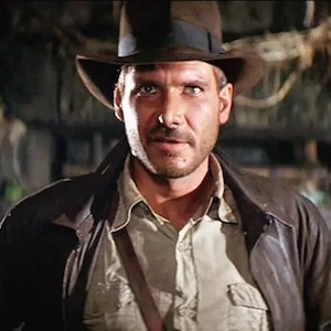 Harrison Ford wearing a hat, leather jacket, and tan shirt in Indiana Jones