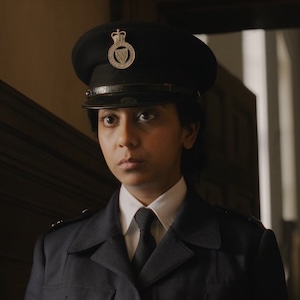 Anjana Vasan as Gladys Moss in Wicked Little Letters wears a black police uniform and cap