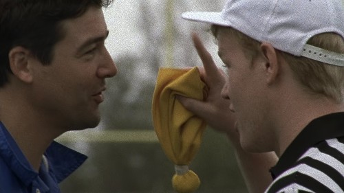 Coach and Landry (in a referee shirt and white baseball hat) face off with Landry holding up a yellow flag