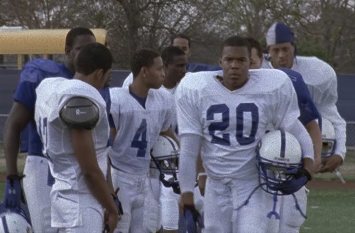 Smash, wearing his football uniform with his helmet in his hand, heads off the field follows by other Black players