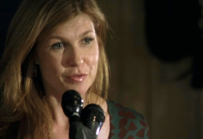 Tami Taylor on the microphone, smiling out into an off-screen crowd