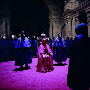 A scene with masked figures wearing capes and gathering inside an old building