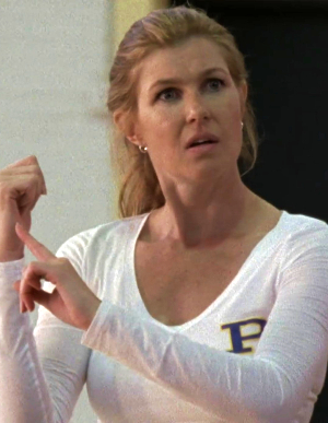 Connie Britton as Tami Tyalor, in a white long-sleeved tee-shirt with the purple Panther P in the corner, her blonde hair in a sporty pony tail, pointing as she coaches on the volleyball court