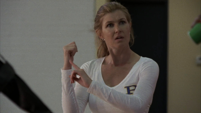 Connie Britton as Tami Tyalor, in a white long-sleeved tee-shirt with the purple Panther P in the corner, her blonde hair in a sporty pony tail, pointing as she coaches on the volleyball court