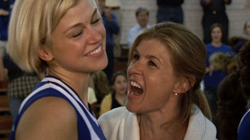 A smiling Adrienne Palicki as Tyra Collette, in a volleyball uniform with a cute blonde bob, on the volleyball court, being hugged by an ecstatic Connie Britton as Tami Tyalor, in a white sweater.