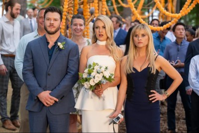 Jimmy Tatro, a white man with brown hair and a beard in a blue suit; Meredith Hagner, a pretty blonde white woman in a wedding dress; Reese Witherspoon, a pretty blonde woman who looks annoyed