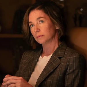 Julianne Nicholson as Sinatra wearing a brown blazer with a quizzical look on her face.
