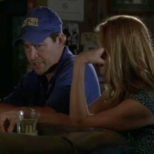 Eric, a middle-aged white man in a blue jacket and hat sits at a bar talking to Tami, a red-haired woman with her back to the camera