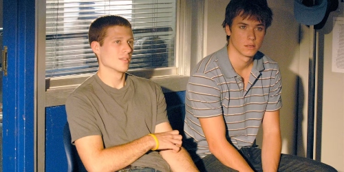 two brown-haired white teenage boys sit in chairs next to an office door