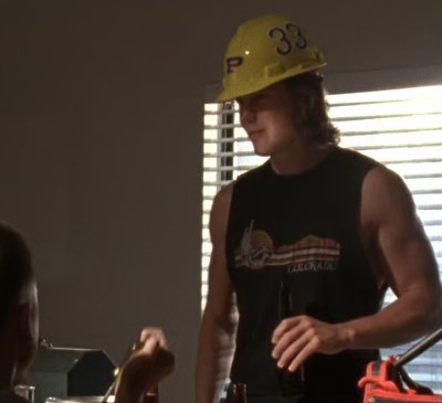 Tim Riggins, wearing a yellow hard hat with 33 on it and holding a beer