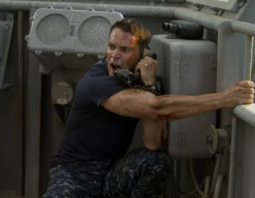 Taylor Kitsch, arm outstretched and huge bicep flex, shouting on the phone on a battleship